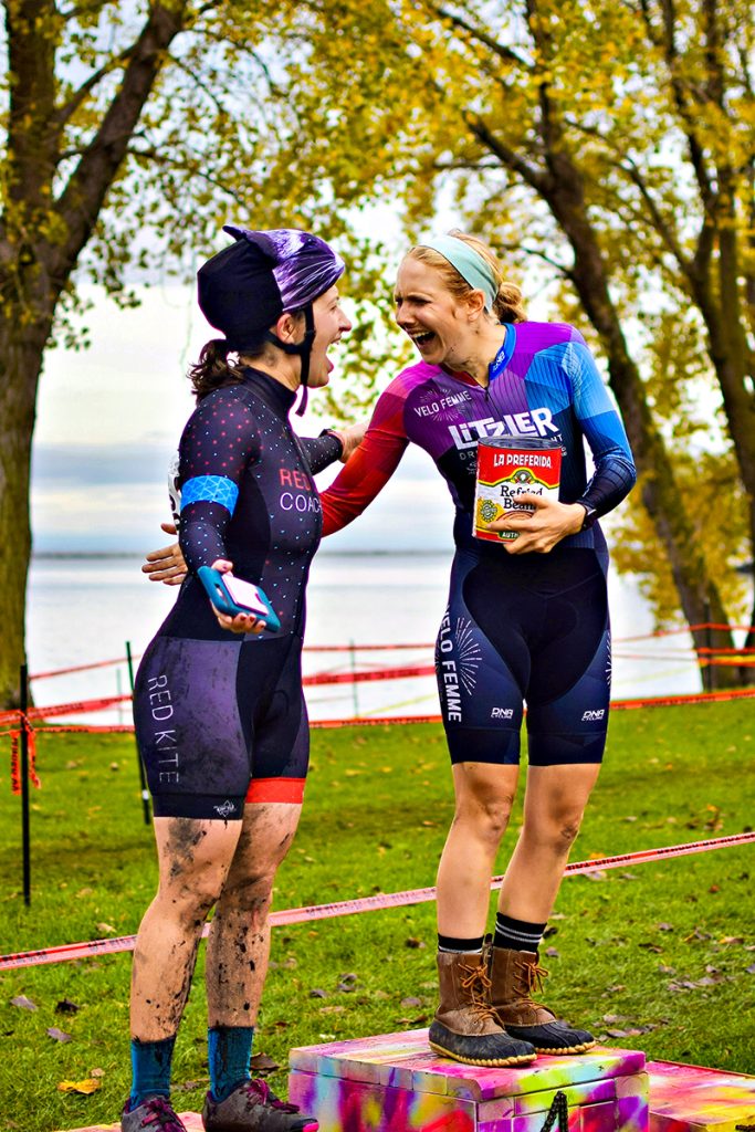 Two women share the podium after a mountain bike race and congratulate each other happily.