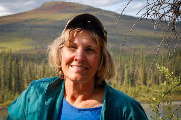 Jean Aspen in the Alaskan wilderness, wearing a ball cap and smiling at the photographer